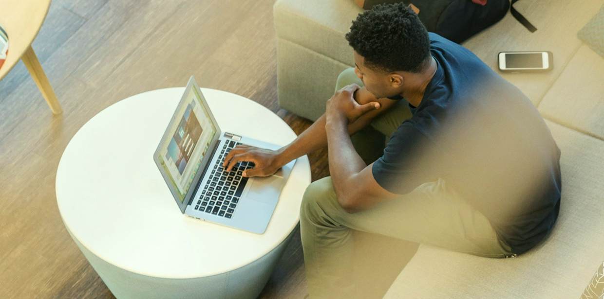 A man sitting on a couch browsing on a laptop