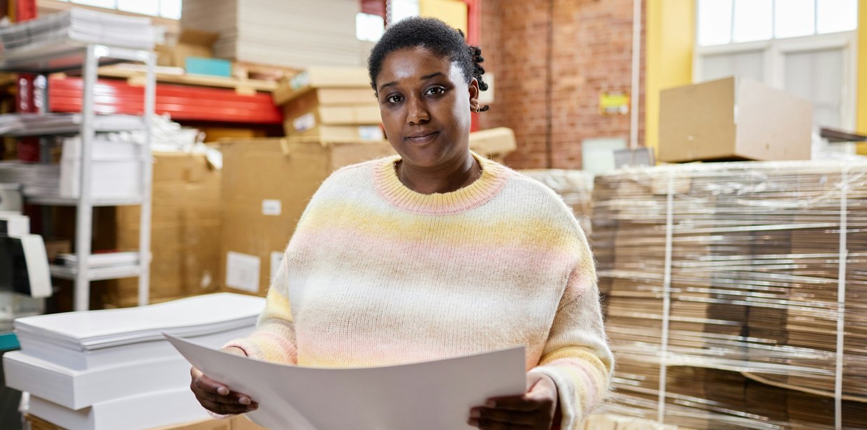 A woman holding a large sheet of paper in a work facility