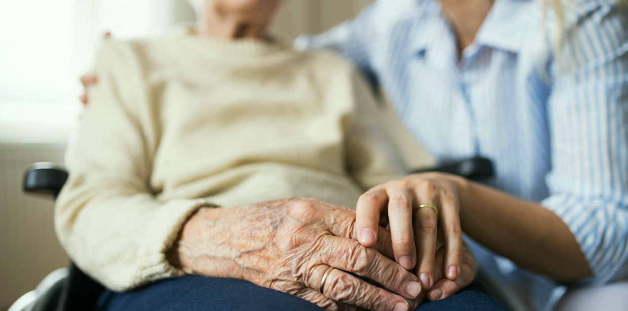 A caregiver holding hands with an elderly person seated in a wheelchair