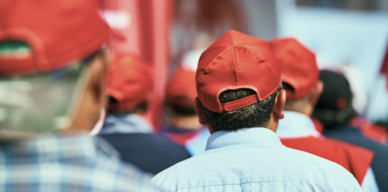 Crowd of workers in red hats standing with their backs to the camera