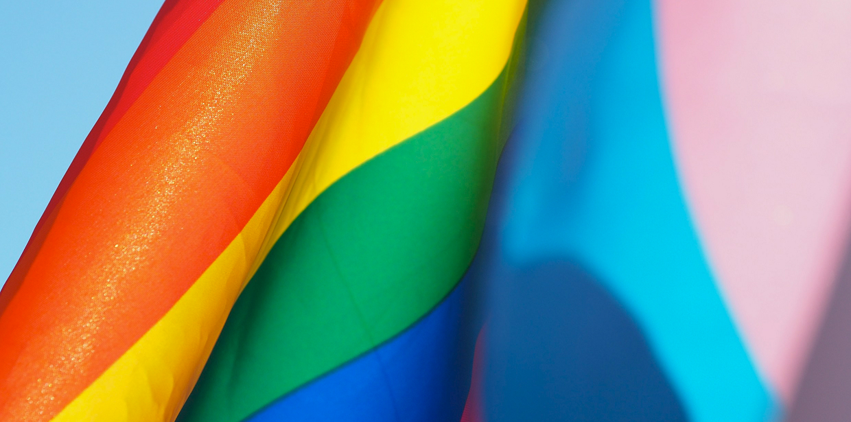 Rainbow Pride and transgender Pride flags waving against a blue sky