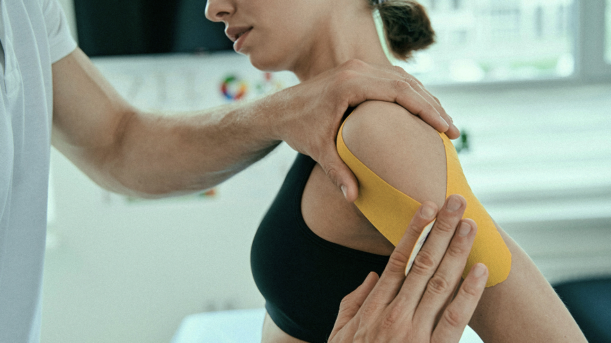 Physiotherapist applying kinesiology tape on a shoulder