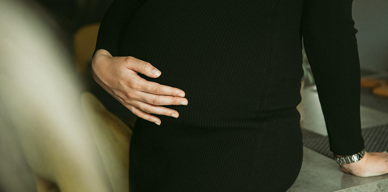 Pregnant woman in a black dress holding a hand on her bump