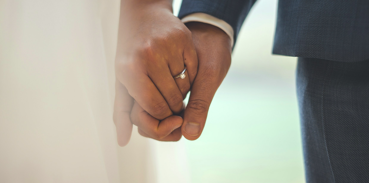A couple holding hands, with a diamond wedding ring visible