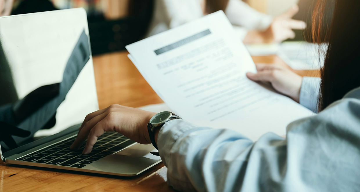 Woman holding documents while working on a laptop