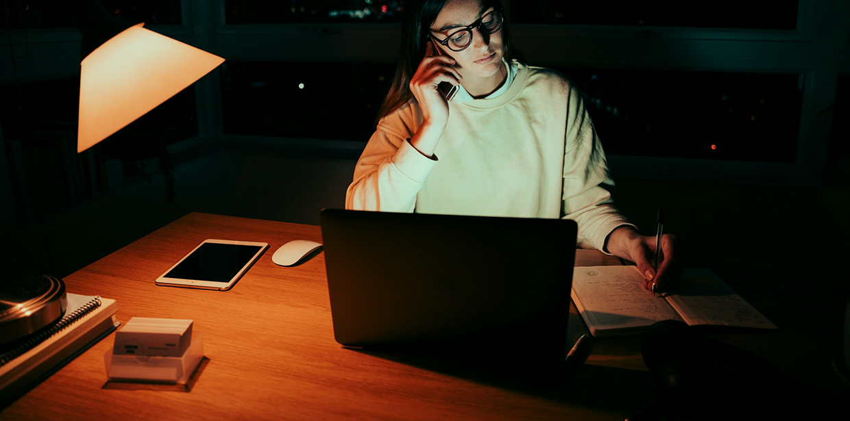 Woman talking on the phone while working late at a laptop